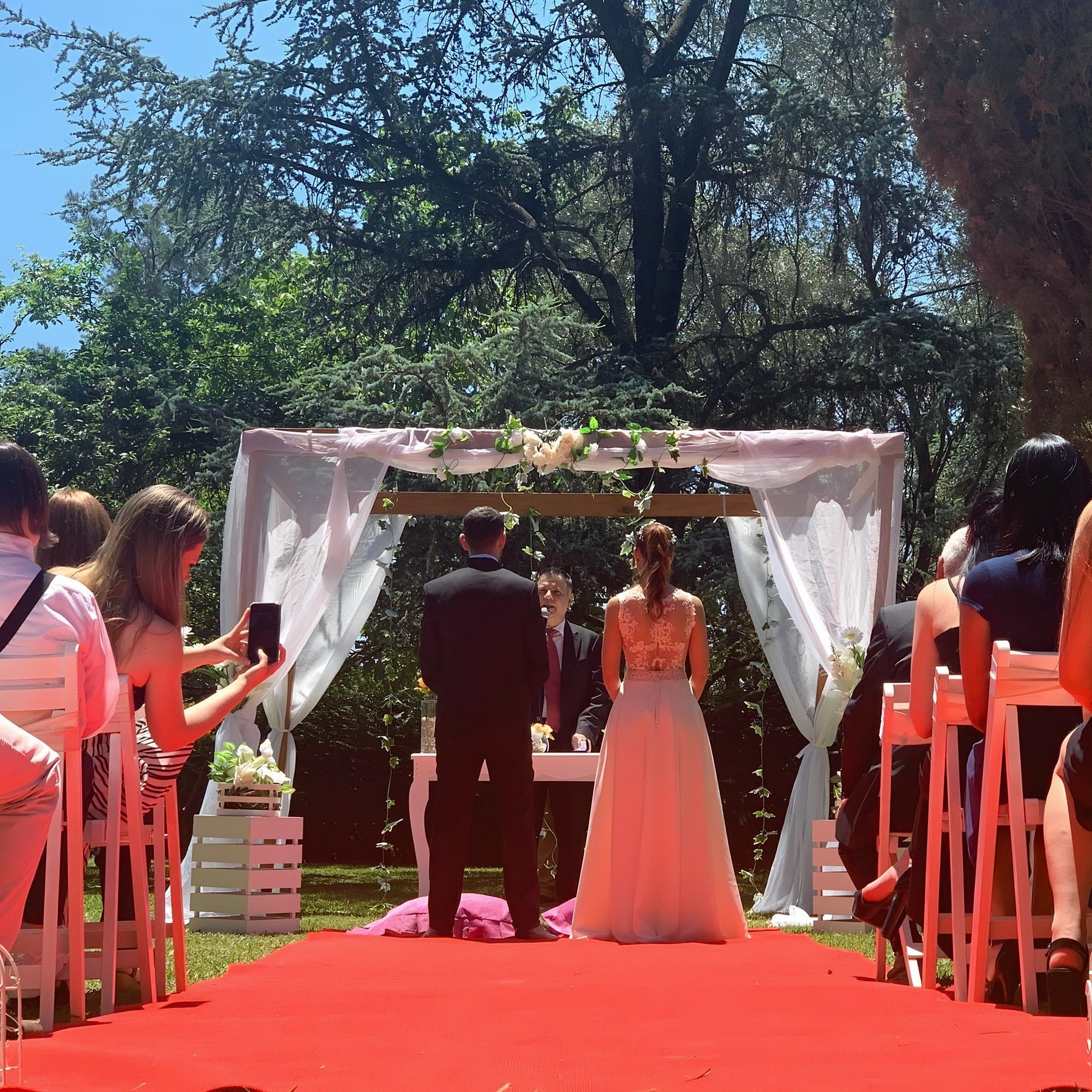 Novios en el arco de la ceremonia sobre la alfombra roja, entre los invitados
