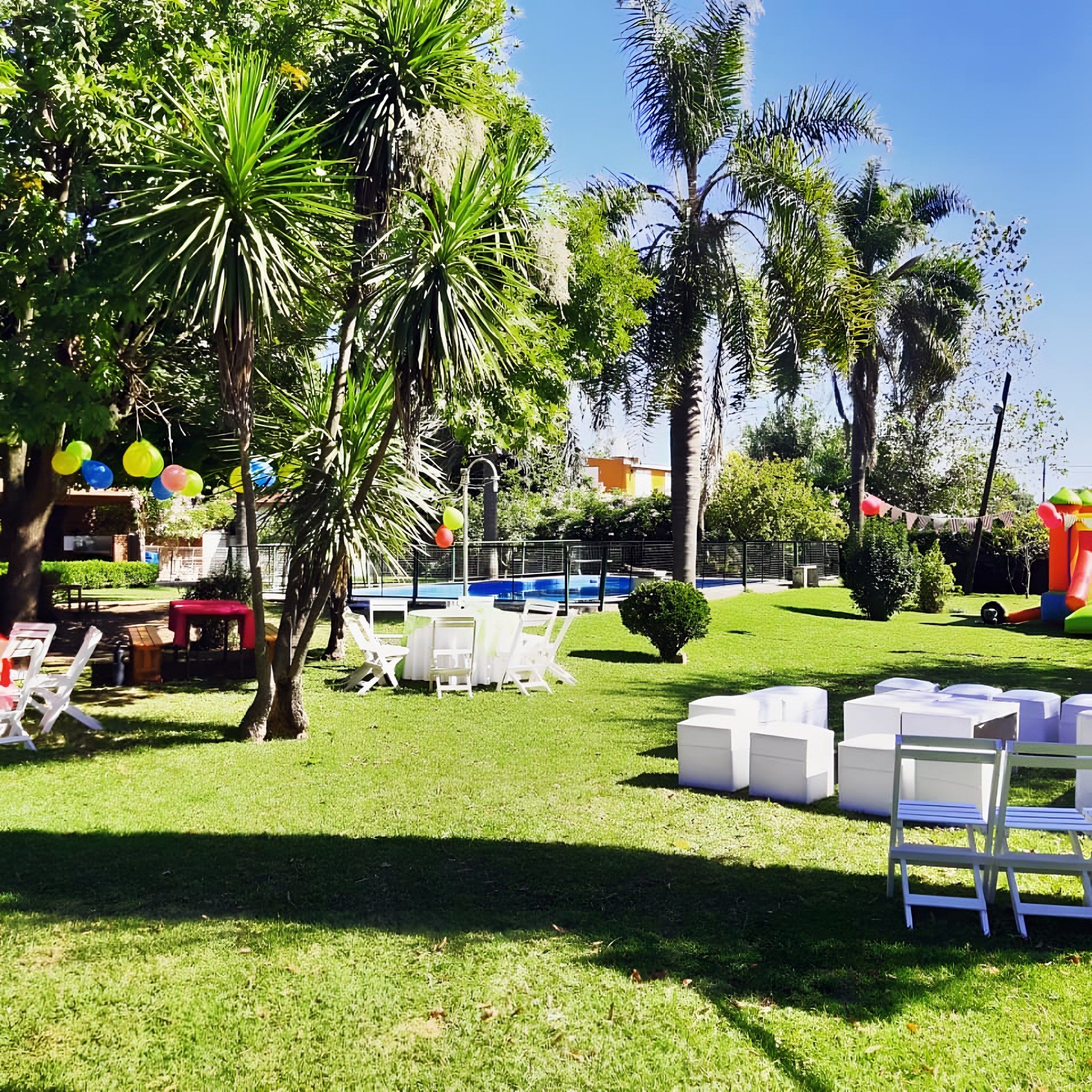 Cumpleaños en el parque con globos de colores, sillas blancas y pufs