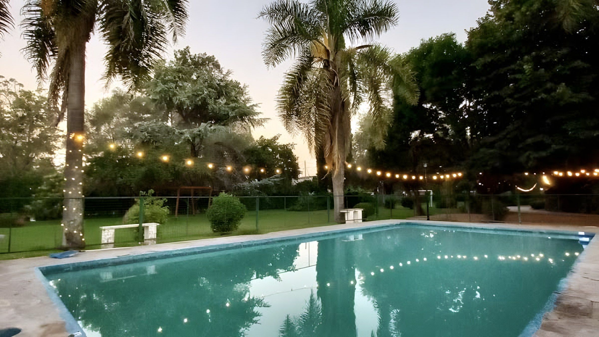 Pileta de la quinta al atardecer con guirnaldas de luces entre las palmeras